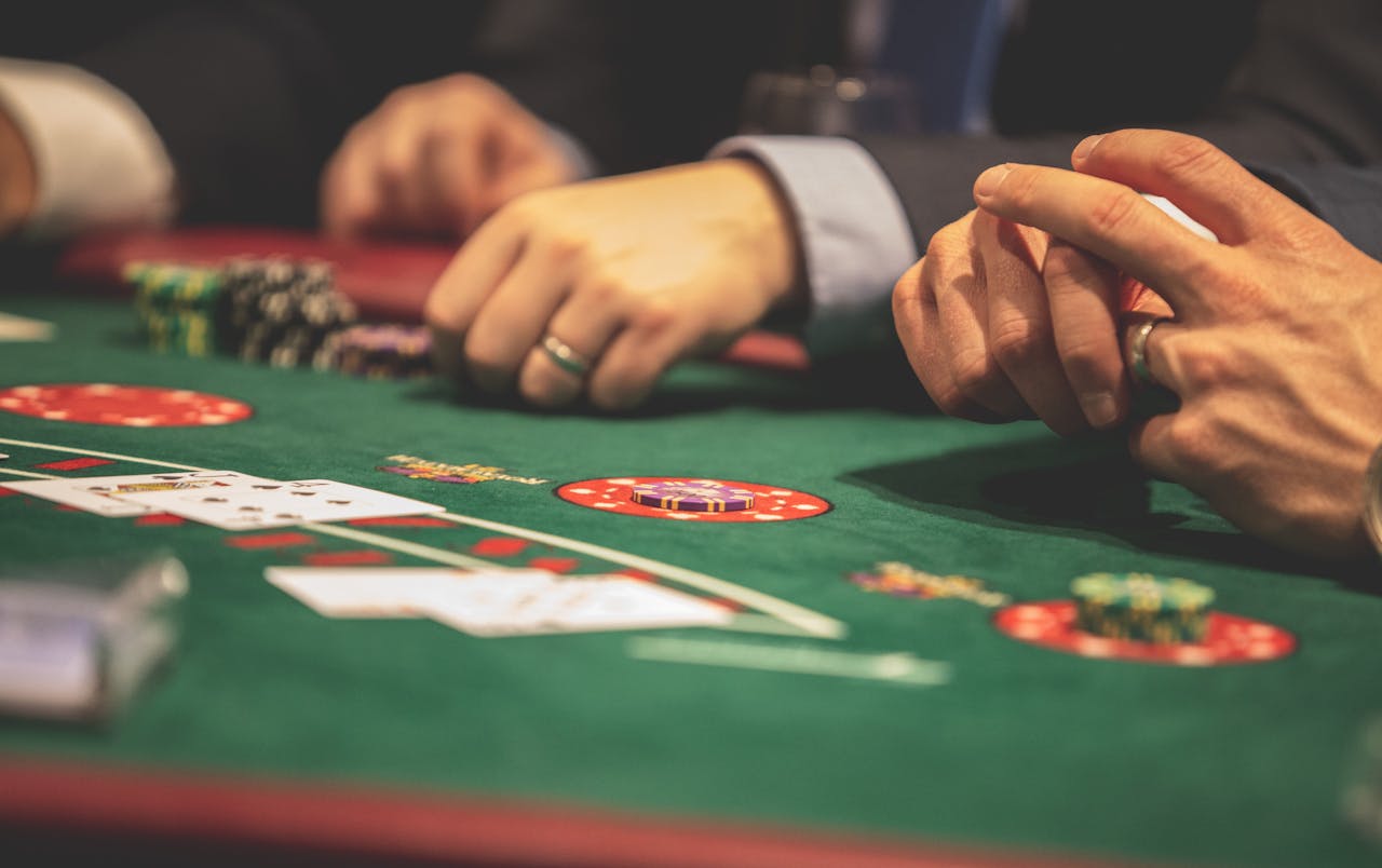 about-us-01 Hands playing blackjack in a casino setting with cards and chips on a green table.