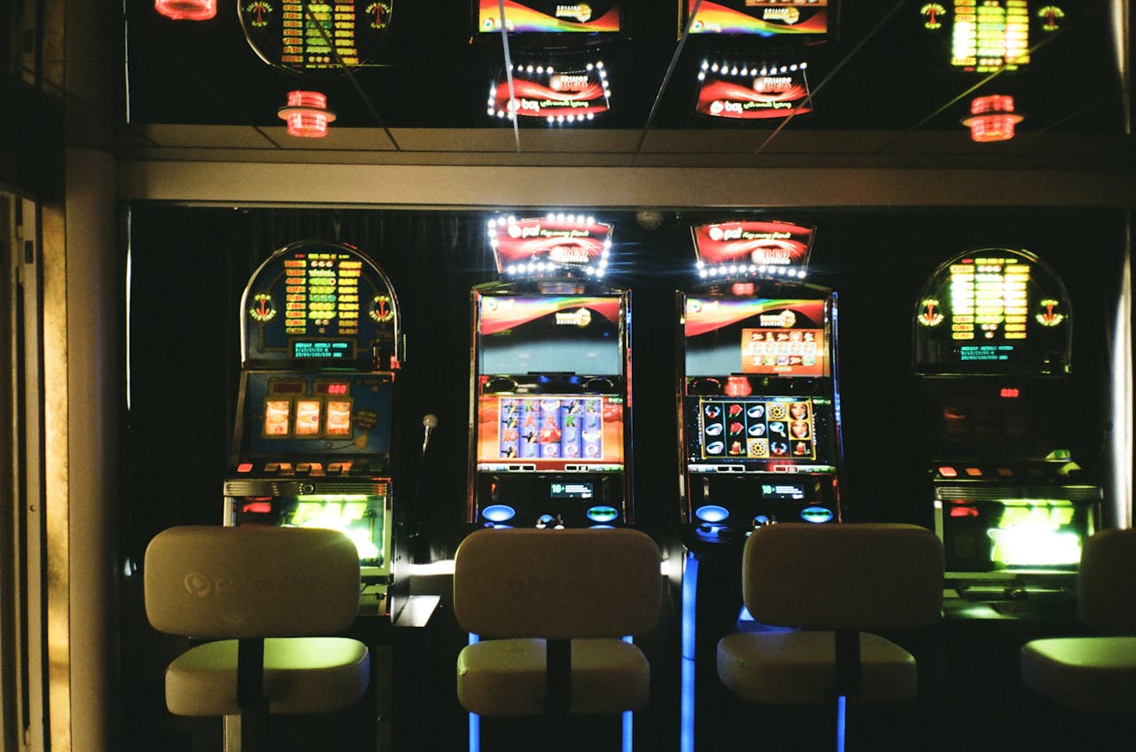gallery-03 Slot machines in a dimly lit casino with reflective ceiling and empty chairs.