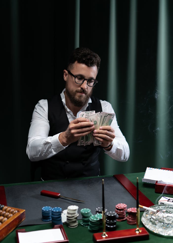 gallery-05 A man at a casino table counting money surrounded by poker chips.